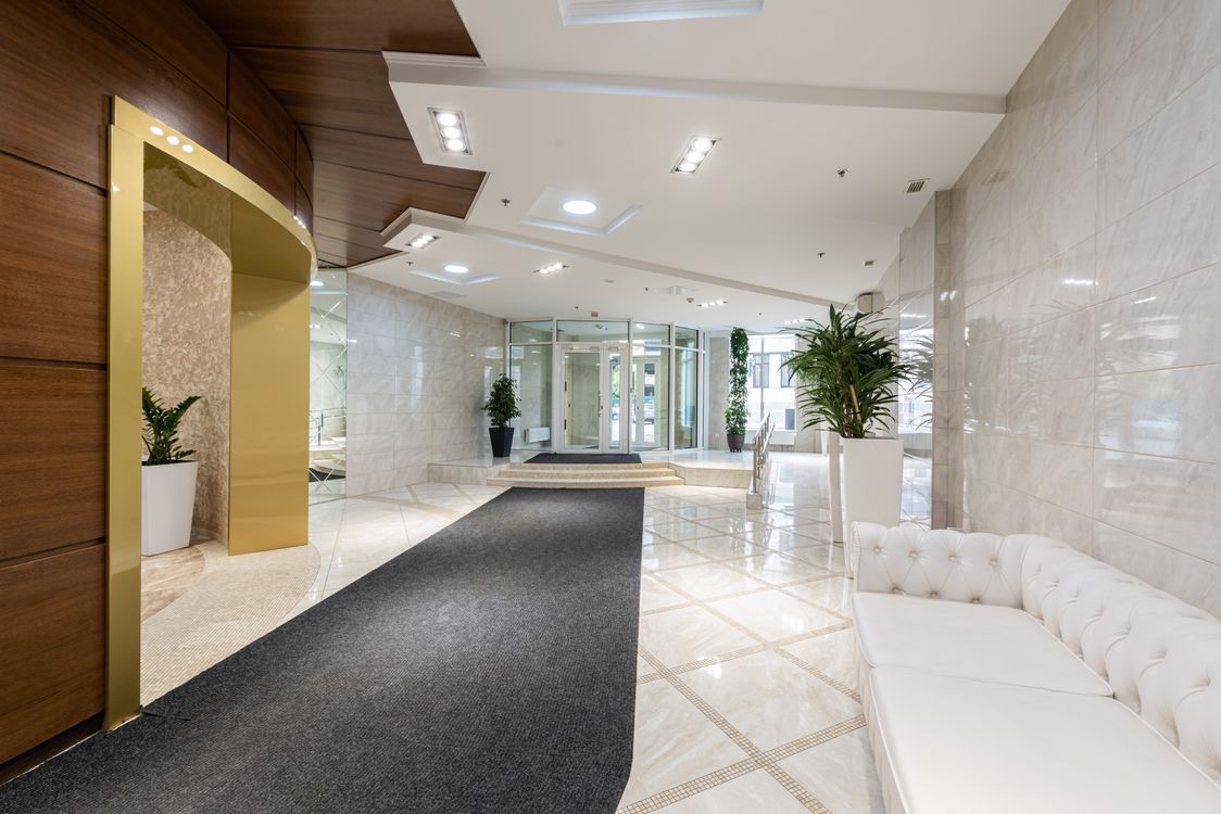 Illustrative bright lobby with a white sofa, marble surfaces and a long dark runner