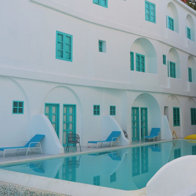 Illustrative resort pool framed by white buildings and turquoise doors